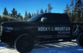 Black Rocky Mountain Plumbing Services truck parked on snow, with trees in the background; business contact info and services listed on the truck's side.