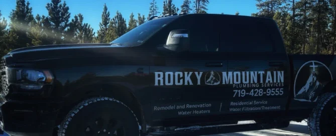 Black Rocky Mountain Plumbing Services truck parked on snow, with trees in the background; business contact info and services listed on the truck's side.