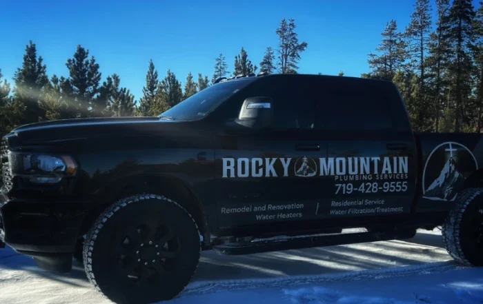 Black Rocky Mountain Plumbing Services truck parked on snow, with trees in the background; business contact info and services listed on the truck's side.