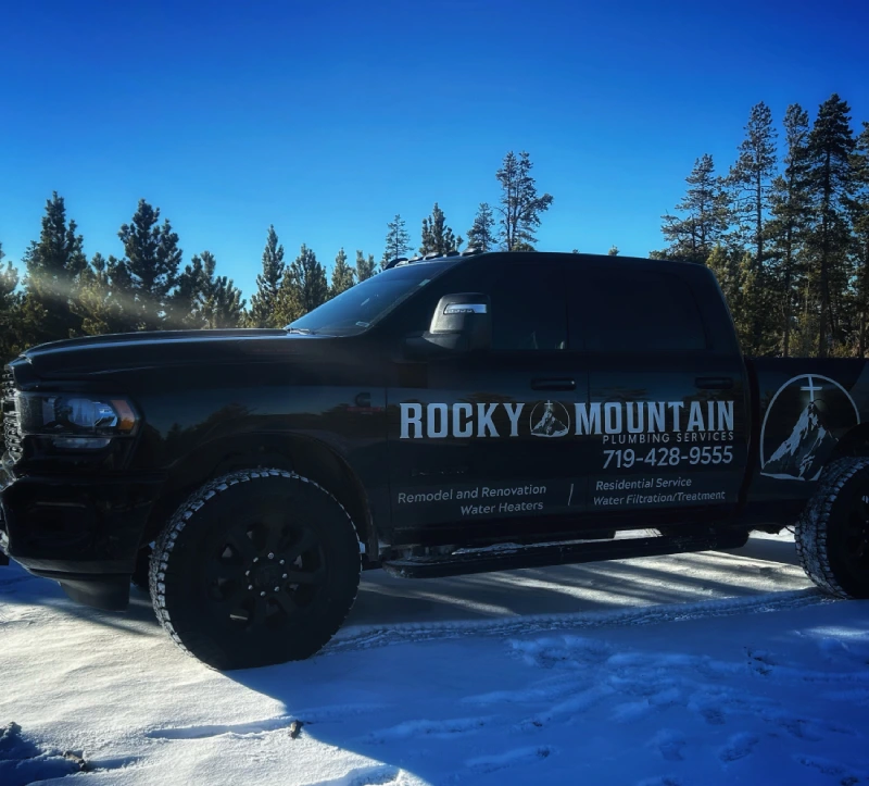Black Rocky Mountain Plumbing Services truck parked on snow, with trees in the background; business contact info and services listed on the truck's side.