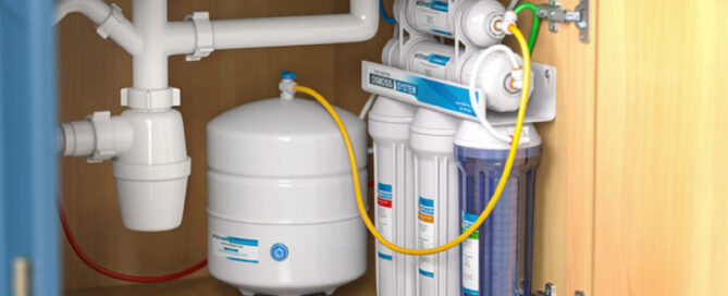 Under-sink water filtration system featuring multiple filter cartridges, a pressurized storage tank, and integrated plumbing beneath a blue kitchen cabinet.